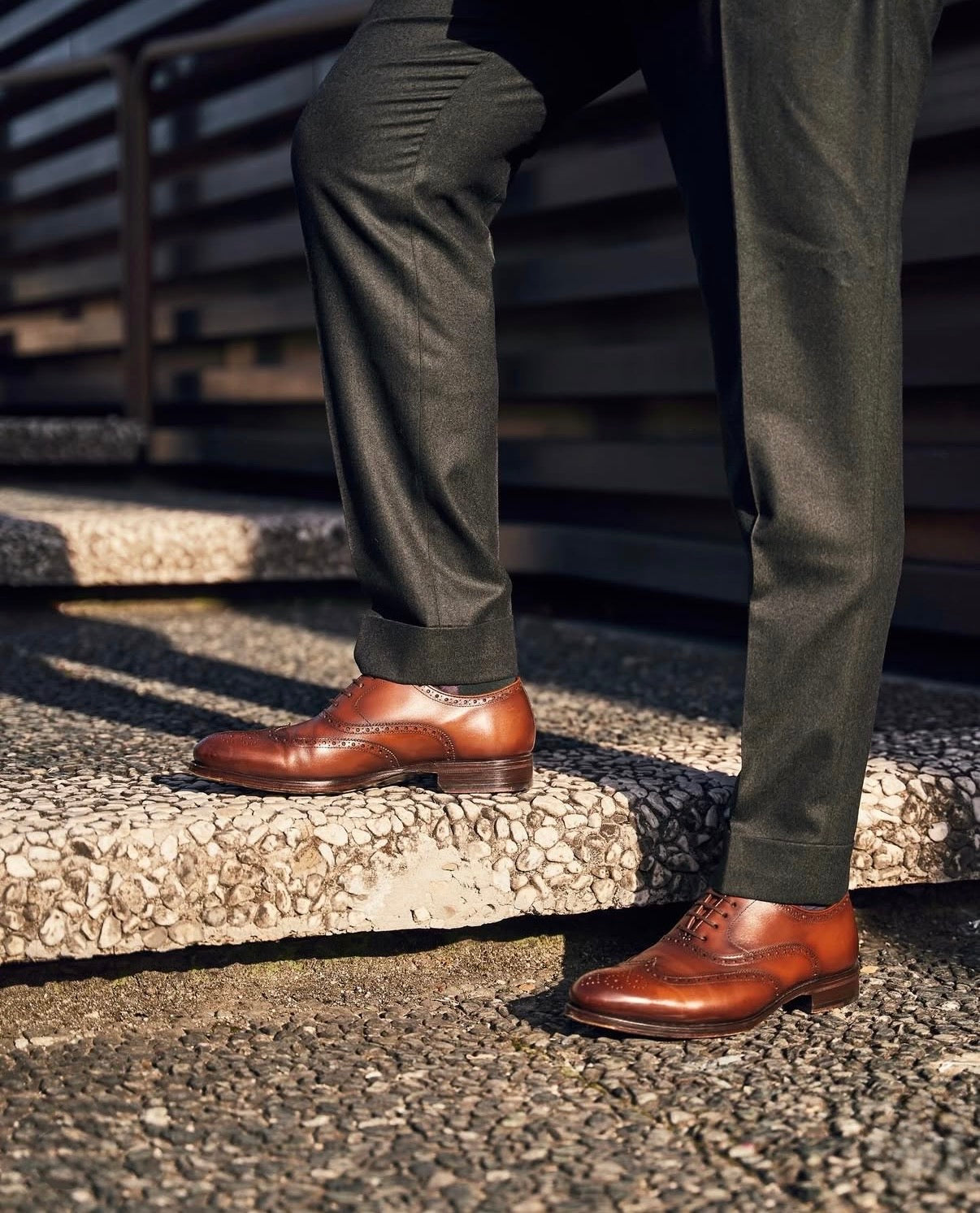 Person wearing brown leather shoes and green pants standing on a stone step.
